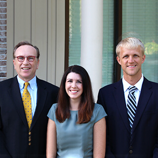 Dr. Laro, Dr. Wade and Dr. Poston smiling straight for a photo in front of our dental office next to a brick wall